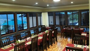 A dining area with multiple tables and chairs, large windows with curtains, and a wooden floor. - Soenam Tsokhang Resort (Paro)