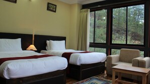 A hotel room with two beds, a chair, a small table, and a large window offering a forest view. - Soenam Tsokhang Resort (Paro)