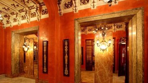 Un amplio pasillo con decoraciones ornamentales en el techo, paredes de mármol y una araña.