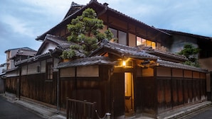 A traditional Japanese building with a wooden exterior, a tiled roof, and a small entrance with a light above it. - HANARé Genmachi (Kyoto)
