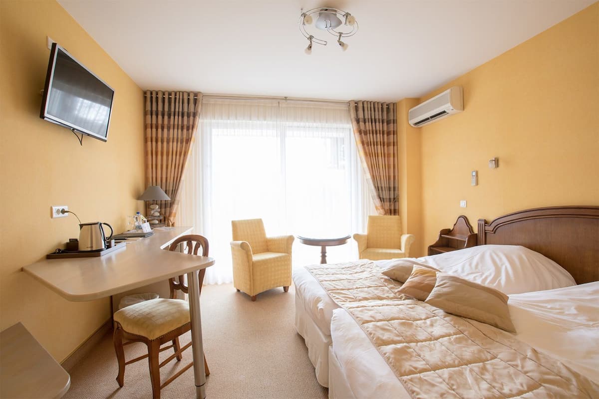 A hotel room with a bed, a desk, two chairs, a television, and a window with curtains.