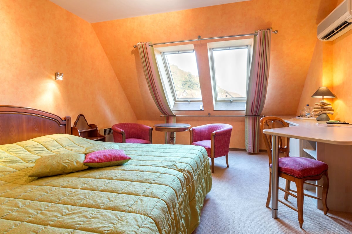 A hotel room with a bed, a desk, two chairs, a small table, and a window with curtains.