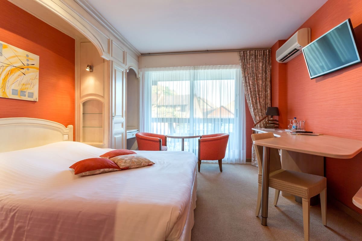 A hotel room with a bed, a desk, two chairs, a TV, and a window with curtains.