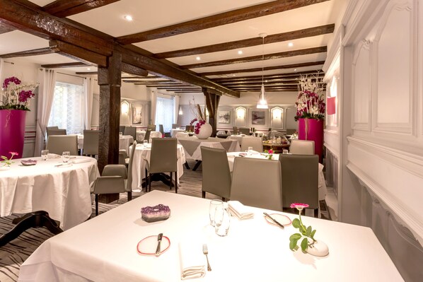 A restaurant with white tablecloths, wooden beams, and floral centerpieces. - Logis Auberge du Cheval Blanc (Westhalten)
