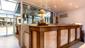 A reception desk with a lamp, a mirror, and a window with a view of the outside. - Logis Auberge du Cheval Blanc (Westhalten)