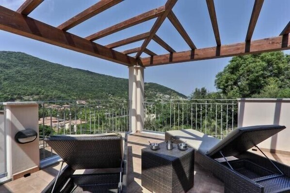A covered outdoor seating area with wicker furniture and a view of a mountainous landscape.