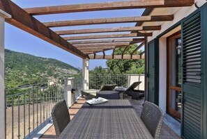 Une terrasse extérieure avec une table et des chaises, une pergola et une vue sur les collines.