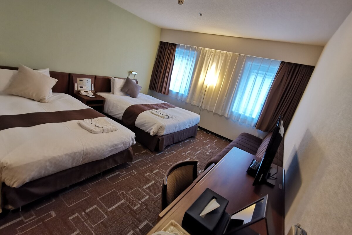 A hotel room with two beds, a desk, a chair, a telephone, and a window with curtains.