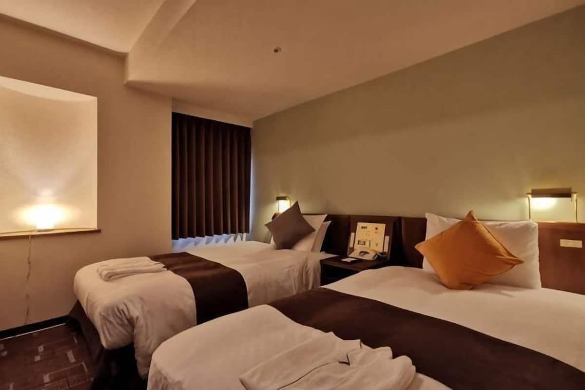A hotel room with two beds, a nightstand, a lamp, and a projector screen.
