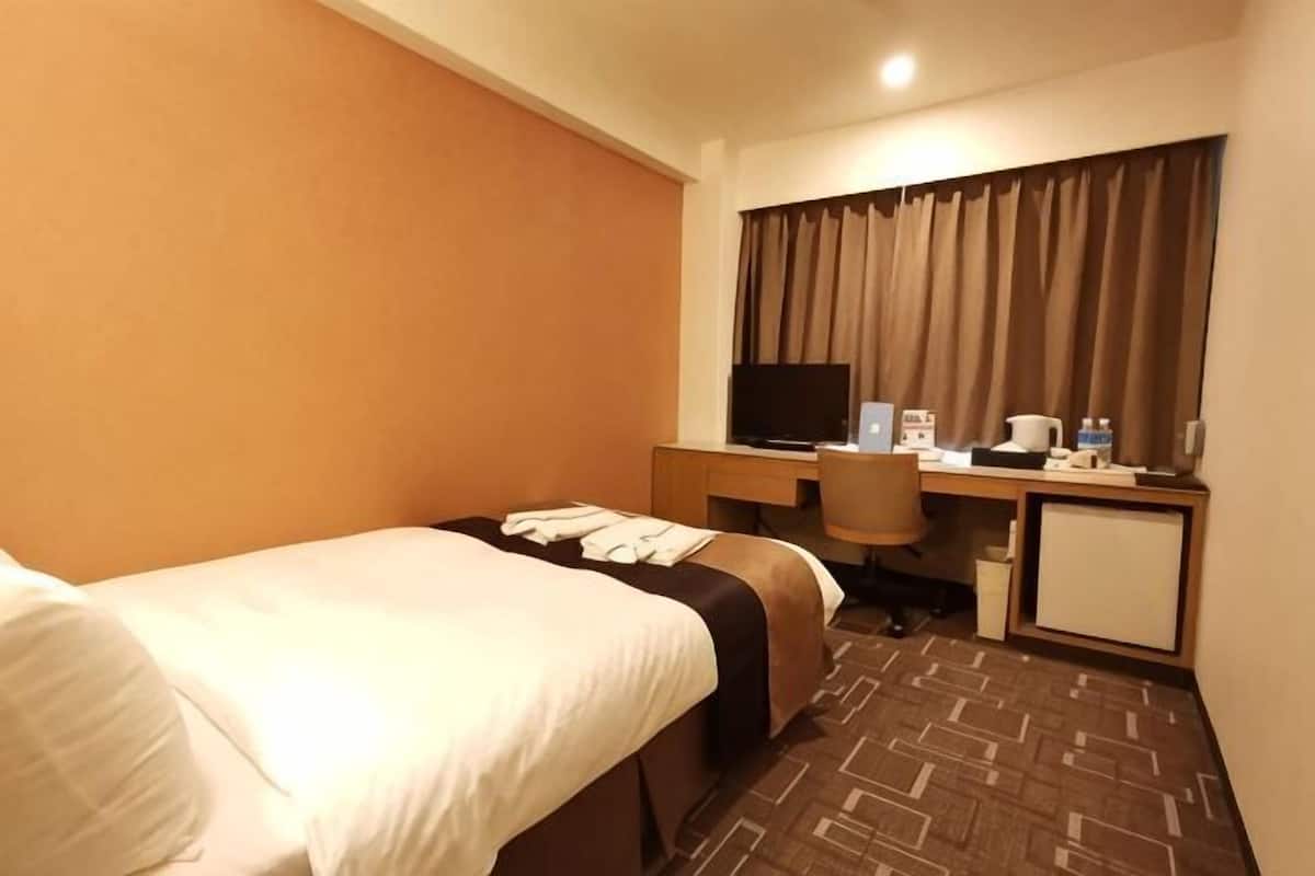 A hotel room with a bed, desk, chair, television, and a small cabinet.