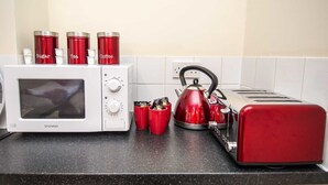 A kitchen with a microwave, toaster, kettle, and red containers labeled sugar, tea, and coffee. - Bradford City Apartments Flat 74 (Bradford)