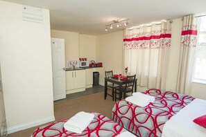 A hotel room with two beds, a small kitchenette, a dining table with chairs, and a window with curtains. - Bradford City Apartments Flat 74 (Bradford)