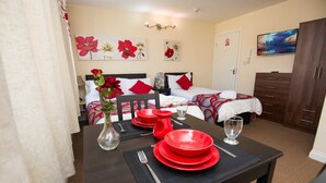 A hotel room with a dining table set for two, a bed with red and white bedding, and a TV on the wall. - Bradford City Apartments Flat 74 (Bradford)