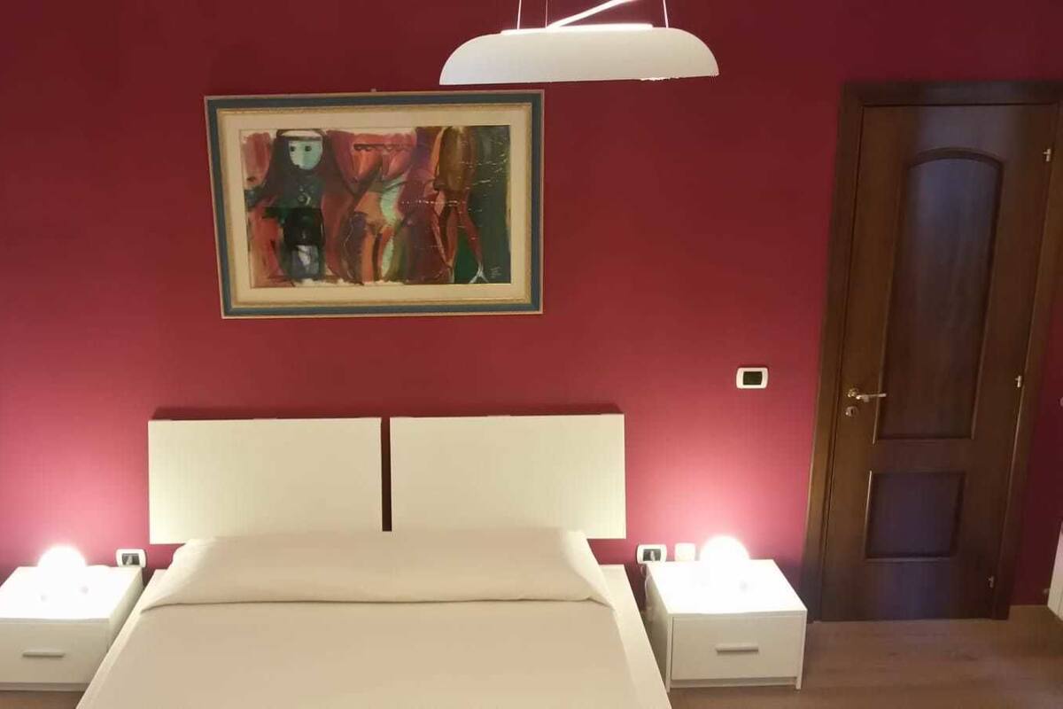 A bedroom with a bed, bedside lamps, a painting on the wall, and a door.
