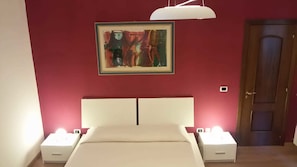 A bedroom with a bed, bedside lamps, a painting on the wall, and a door. - Def House (Reggio Calabria)
