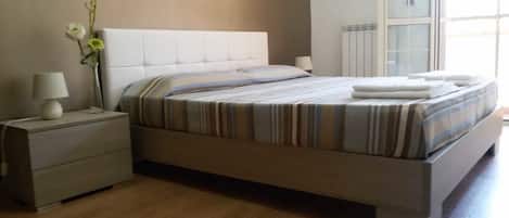 Une chambre à coucher moderne avec un grand lit, une table de chevet avec une lampe et un vase rempli de fleurs.