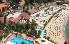 An aerial view of a resort with a swimming pool, beach area with umbrellas, and a road. - Def House (Reggio Calabria)