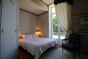 Un dormitorio con cama, una silla, un ventanal con cortinas y un radiador.