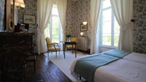 Un dormitorio con papel tapiz floral, una cama, un escritorio con silla y un radiador.