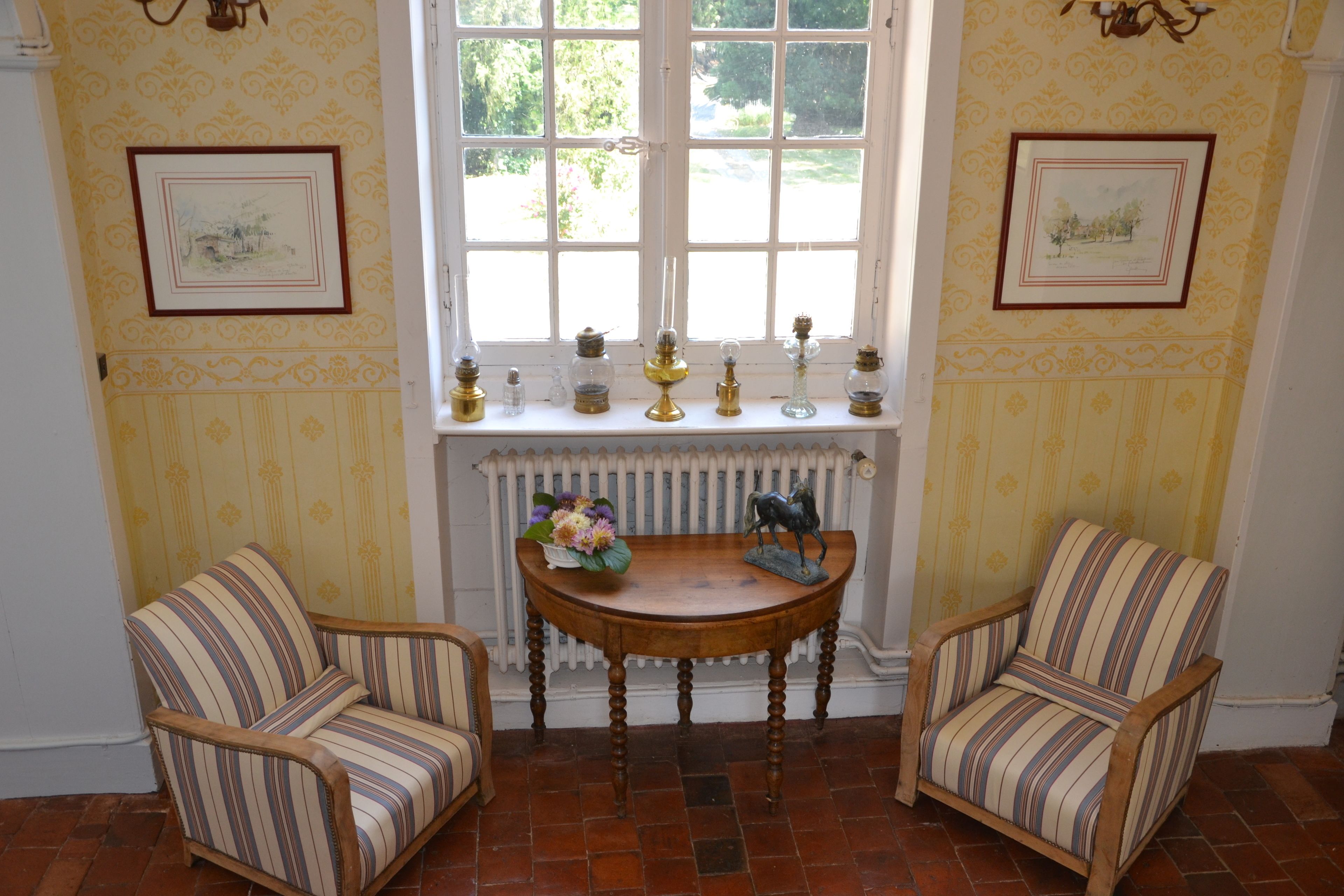Una stanza con due poltrone a righe, un tavolo di legno con un vaso di fiori e una finestra con un termosifone sottostante.