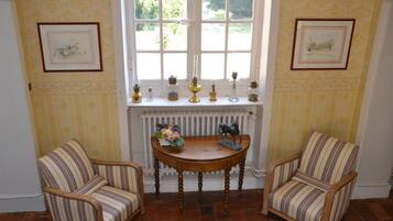 Ein Zimmer mit zwei gestreiften Sesseln, einem Holztisch mit Blumenvase und einem Fenster mit Heizkörper darunter.