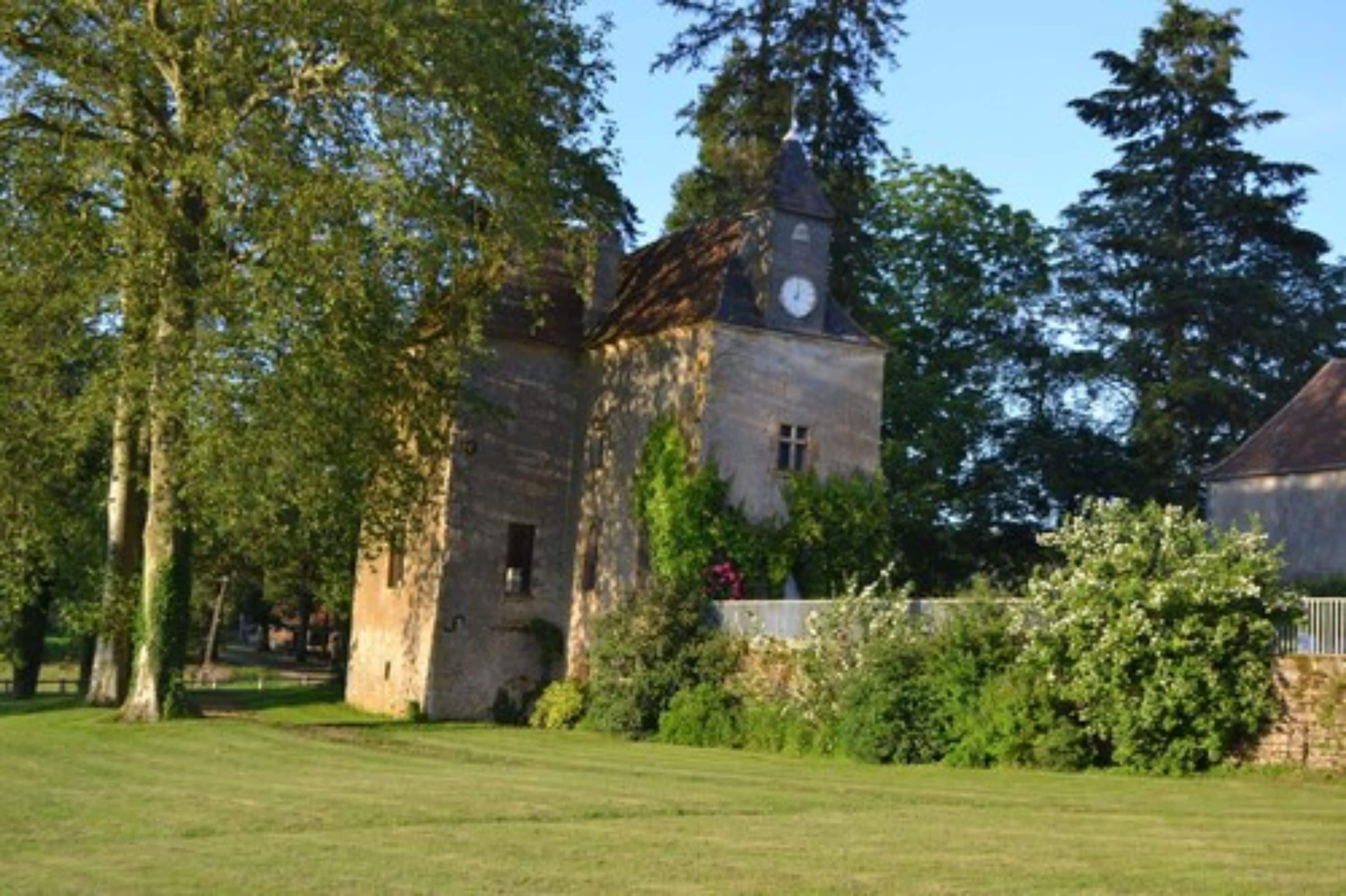 A stone building with a clock tower, surrounded by lush greenery and trees.