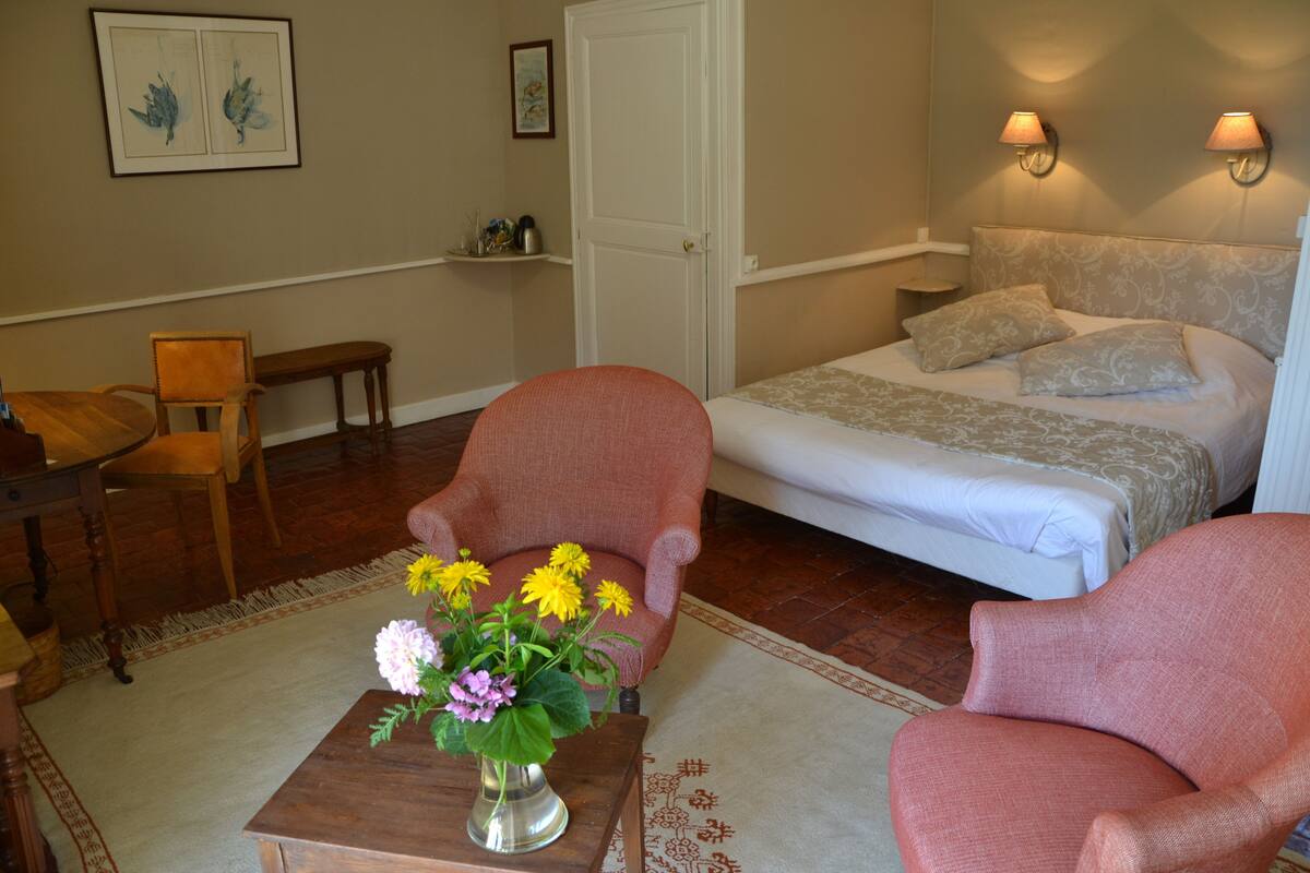 Un dormitorio con una cama, dos sillas, una mesa con un florero y una puerta.