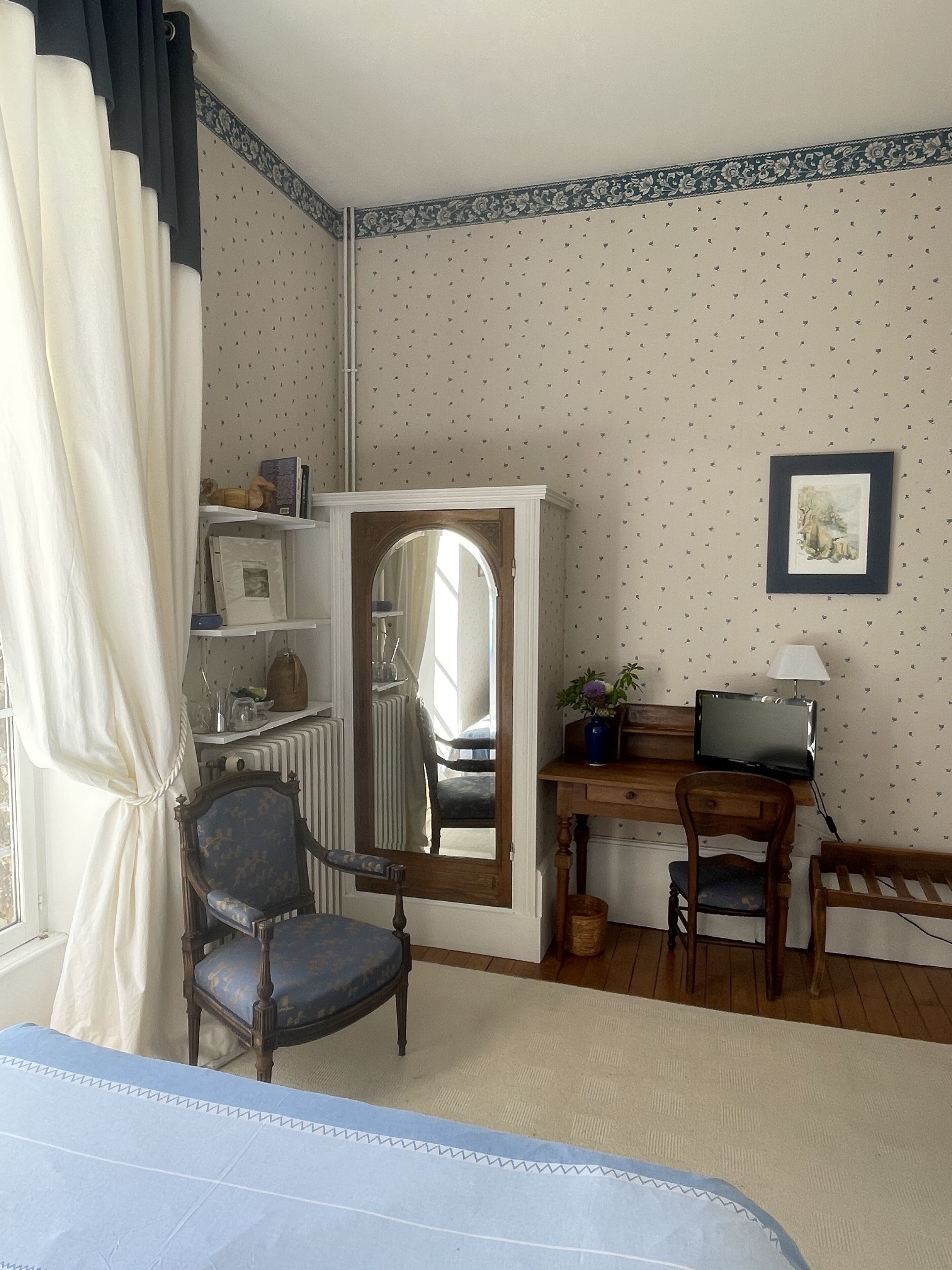 Una habitación con una cama, un escritorio con computadora, una silla, un espejo y un radiador.