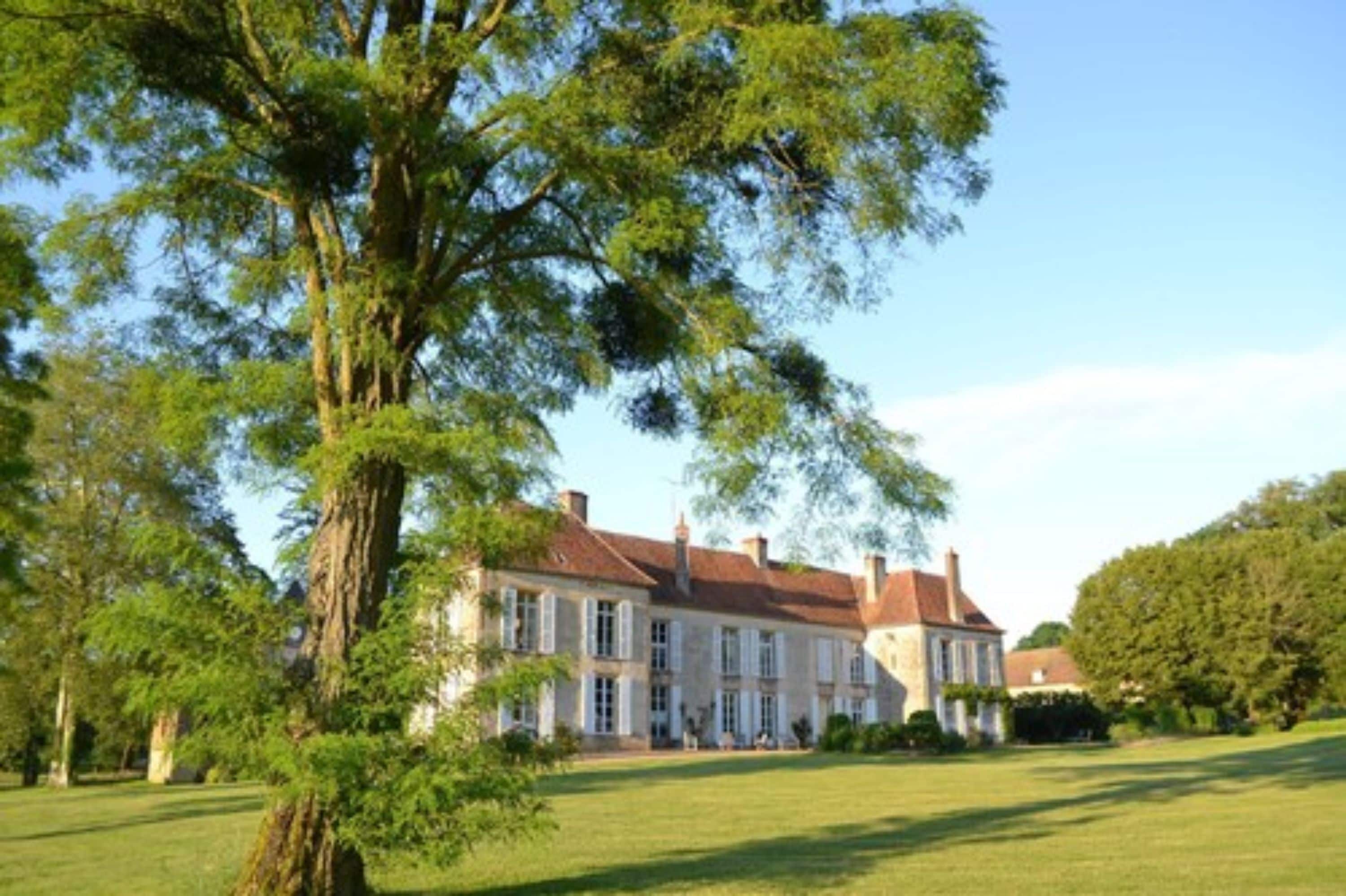 A large, historic building with a symmetrical facade, surrounded by lush greenery and a well-maintained lawn.