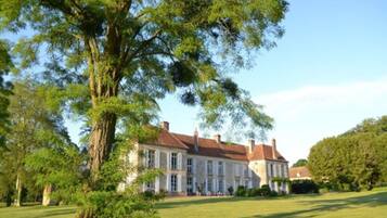 A large, historic building with a symmetrical facade, surrounded by lush greenery and a well-maintained lawn.