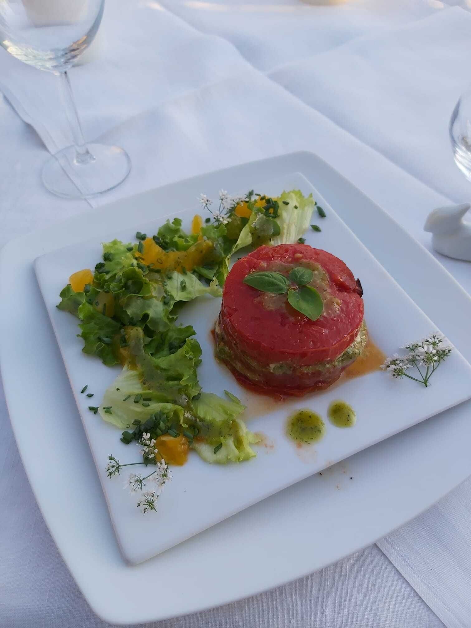 Um prato quadrado branco com um prato de carne vermelha, salada verde e um copo de vinho branco sobre uma toalha de mesa branca.