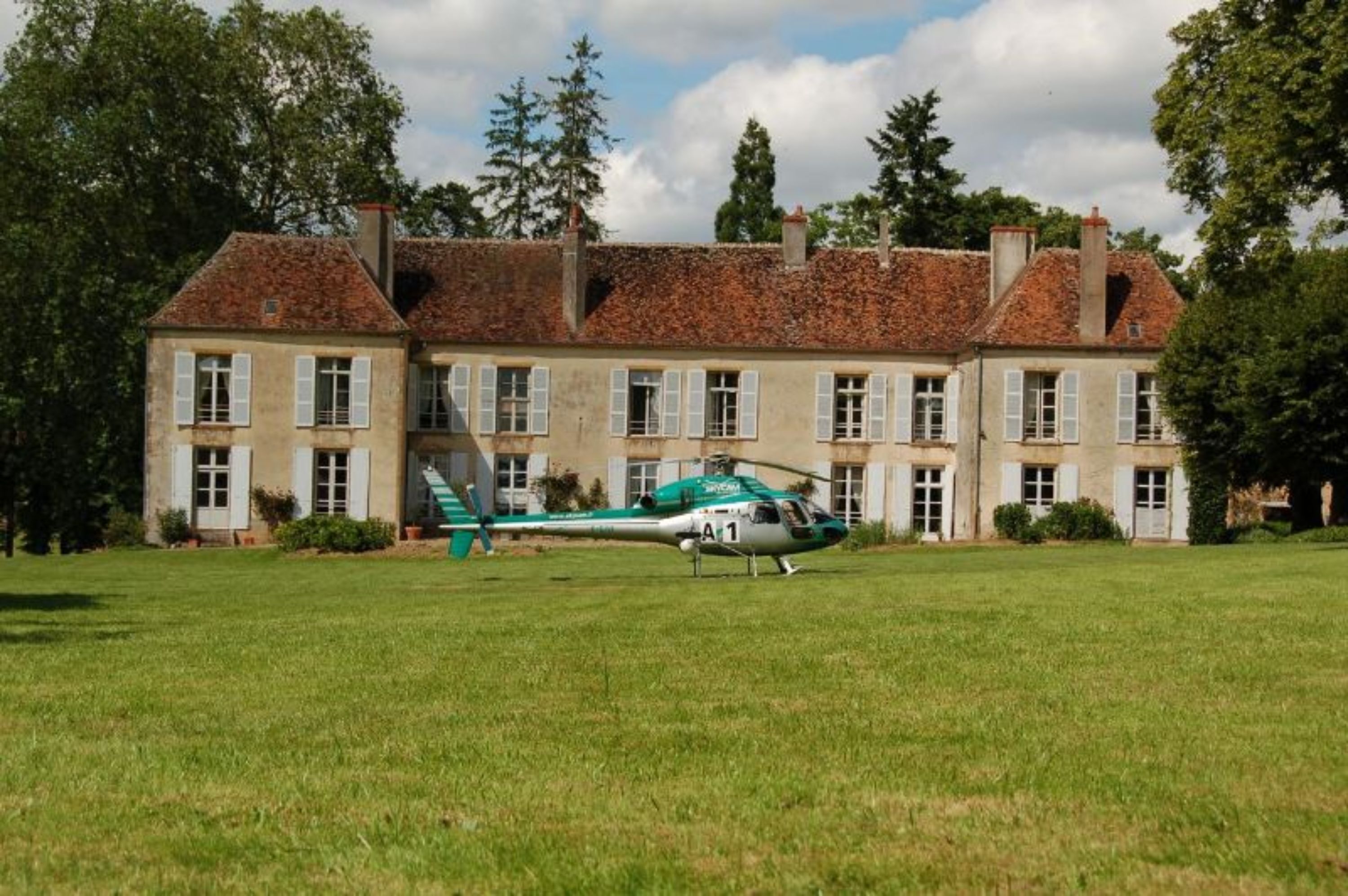 Un edificio grande de dos pisos con un helicóptero verde estacionado frente a él.
