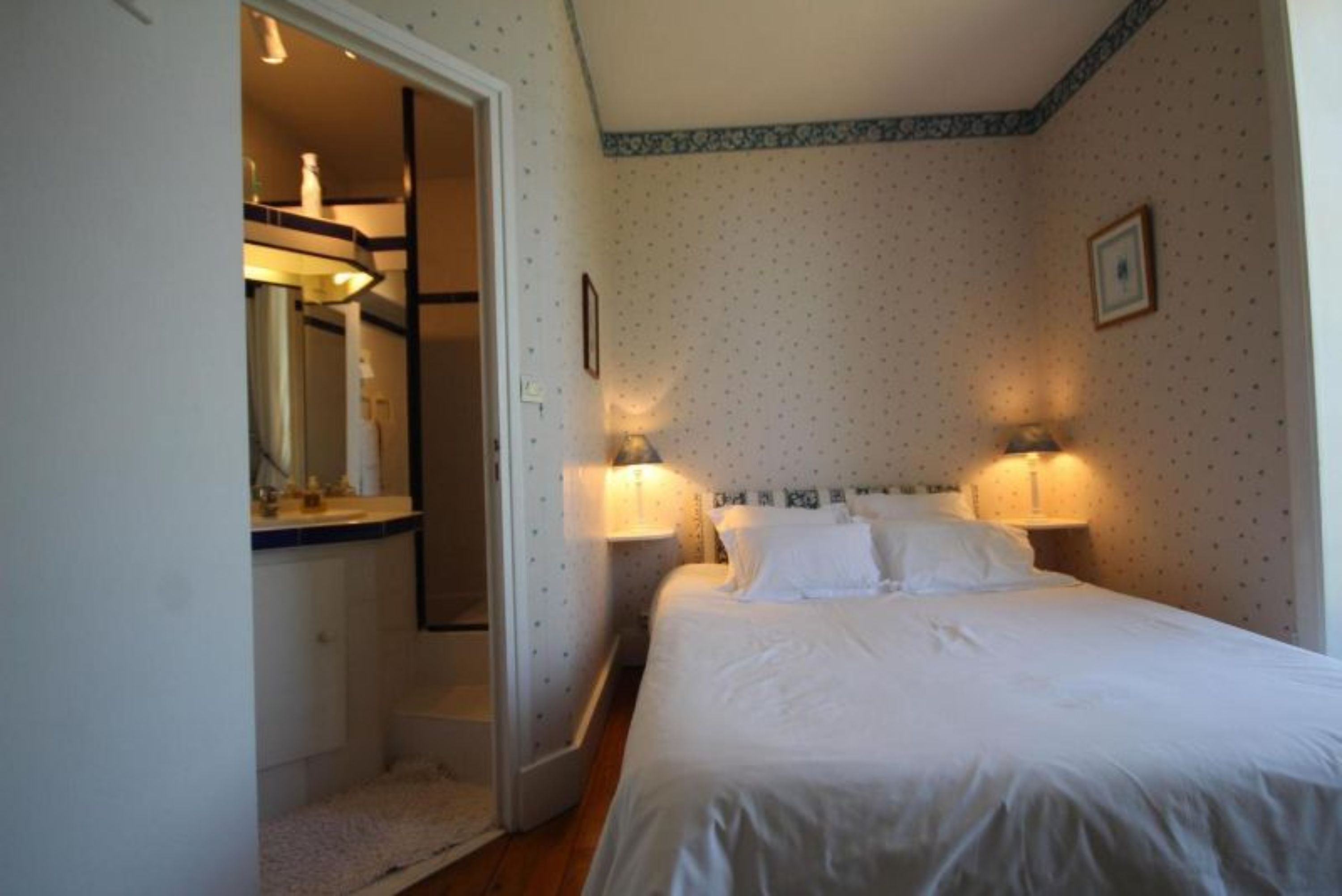 Ein Schlafzimmer mit einem Bett, Nachttischlampen, einem Spiegel und einer Tür zu einem Badezimmer.