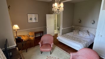 Une chambre à coucher avec un lit, deux fauteuils, une petite table sur laquelle est posé un vase de fleurs, une lampe et un tableau accroché au mur.