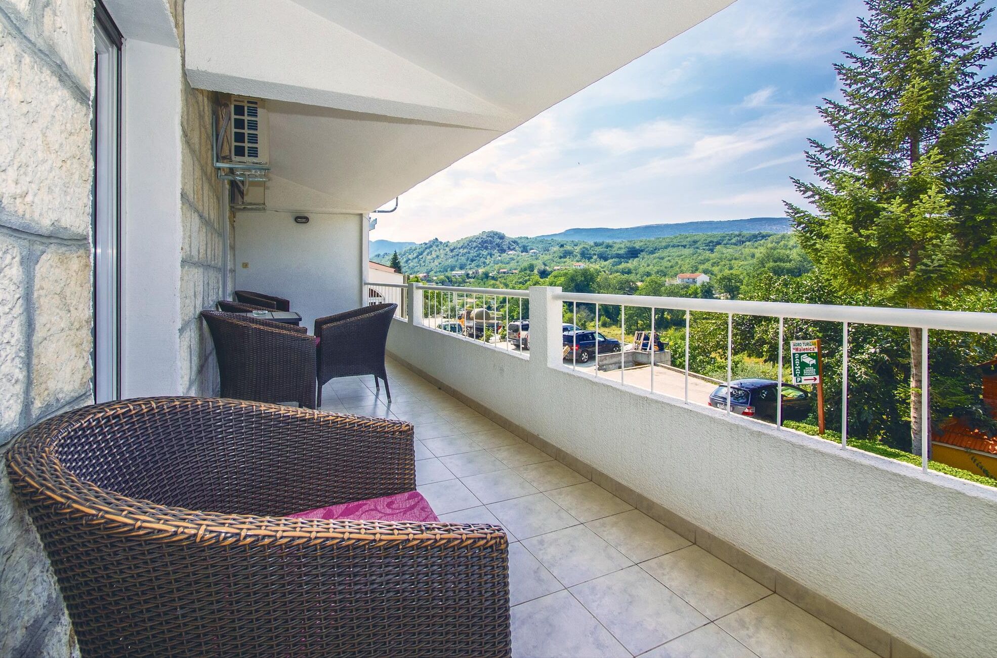 A balcony with wicker furniture, a view of a green landscape, and a sign indicating a parking area.