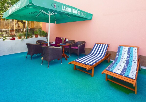 A patio area with a green umbrella, wicker furniture, and striped lounge chairs. - Nice apartment in Ostrvica with WiFi (Ostrvica)