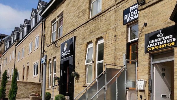 Una hilera de casas urbanas con un letrero que dice 'BUDG ROOM', una escalera y una tienda llamada 'Snooze'.