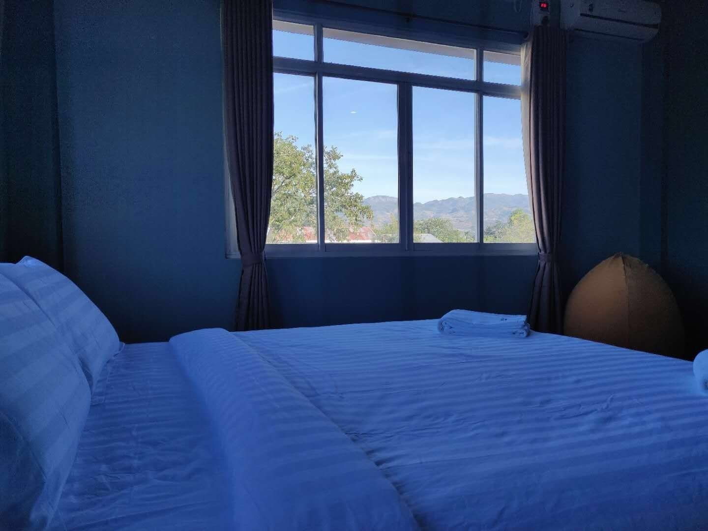 A hotel room with a large bed, a window with curtains, and a view of the outdoors.
