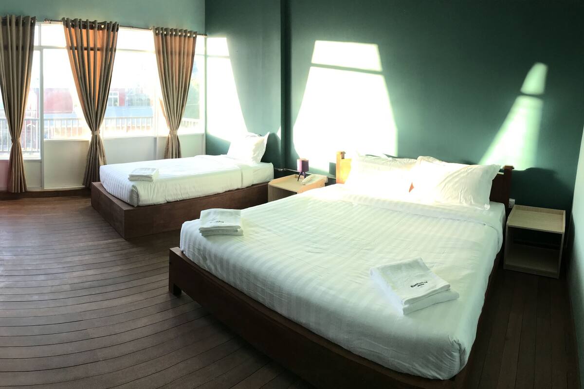 A hotel room with two beds, a wooden floor, a red bean bag, and large windows with curtains.
