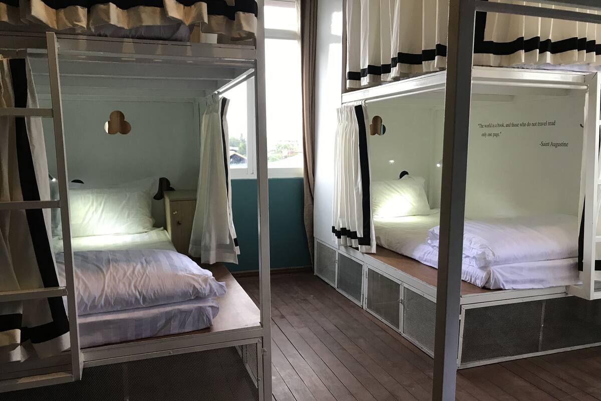 A room with two bunk beds, each with a canopy, a small desk, and a window.