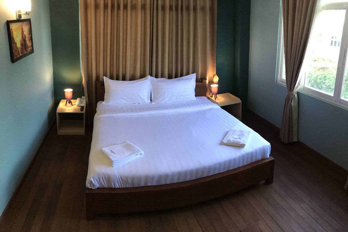 A large bed with white linens, two bedside tables with lamps, and a window with curtains.
