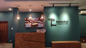 Een receptie met een houten toonbank, een bank en een wandbordje voor BaobaBed Hostel, Cafe & Bar.
