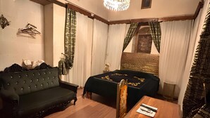 Une pièce chaleureuse avec un plafond en bois, un lustre, un canapé, un lit recouvert d’une courtepointe vert foncé et une table en bois avec une chaise.