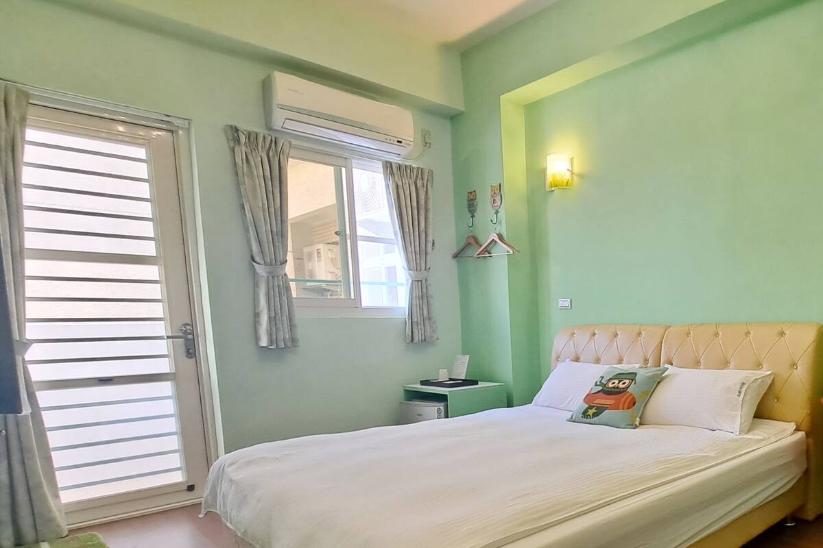 A bedroom with a bed, a nightstand, a chair, and a wall-mounted shelf.