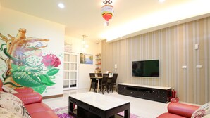 A living room with a sofa, a coffee table, a TV, and a wall with a giraffe mural. - Dao Siang Hai B&B (Taitung)
