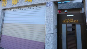A building with a closed shutter and a door with a phone number. - Dao Siang Hai B&B (Taitung)