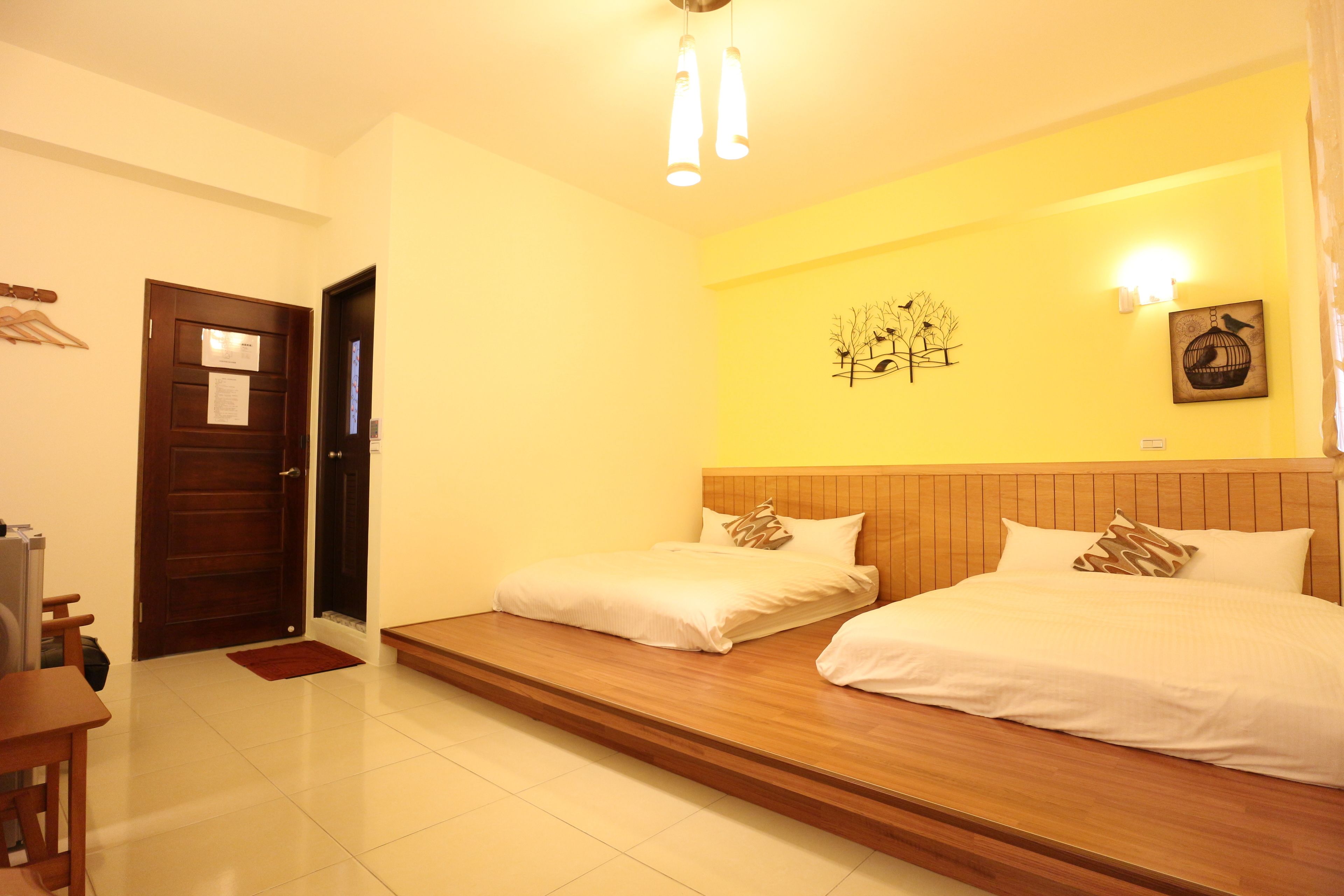 A hotel room with a wooden bed, a wooden headboard, a wall-mounted light fixture, and a door with a notice.