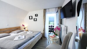 Et hotelværelse med seng, fjernsyn, stol og et lille bord med en bog og blomster.