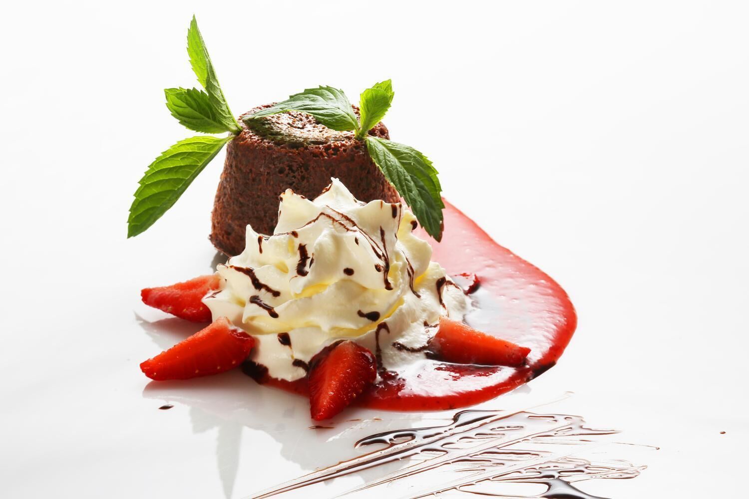 A dessert with a chocolate cake, whipped cream, strawberries, and mint leaves.