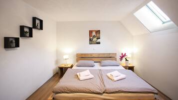 Una camera da letto con un lucernario, un letto con due cuscini, un comodino con una lampada e tre quadri appesi al muro.